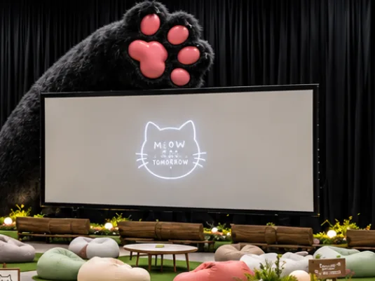 Render of a giant black cat paw reaching over a projection screen above beanbags